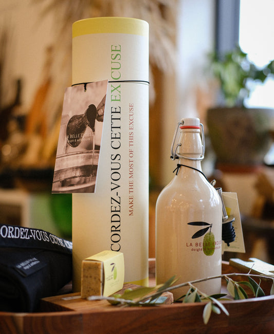La Belle Excuse Greek Heritage Gift Set featuring a ceramic bottle filled with 500 ml of extra virgin green olive oil, a unisex kitchen apron, and rosemary, lemon and coffee kitchen soap.