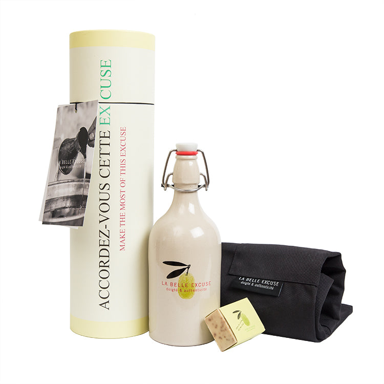 La Belle Excuse Greek Heritage Gift Set featuring a ceramic bottle filled with 500 ml of extra virgin green olive oil, a unisex kitchen apron, and rosemary, lemon and coffee kitchen soap.