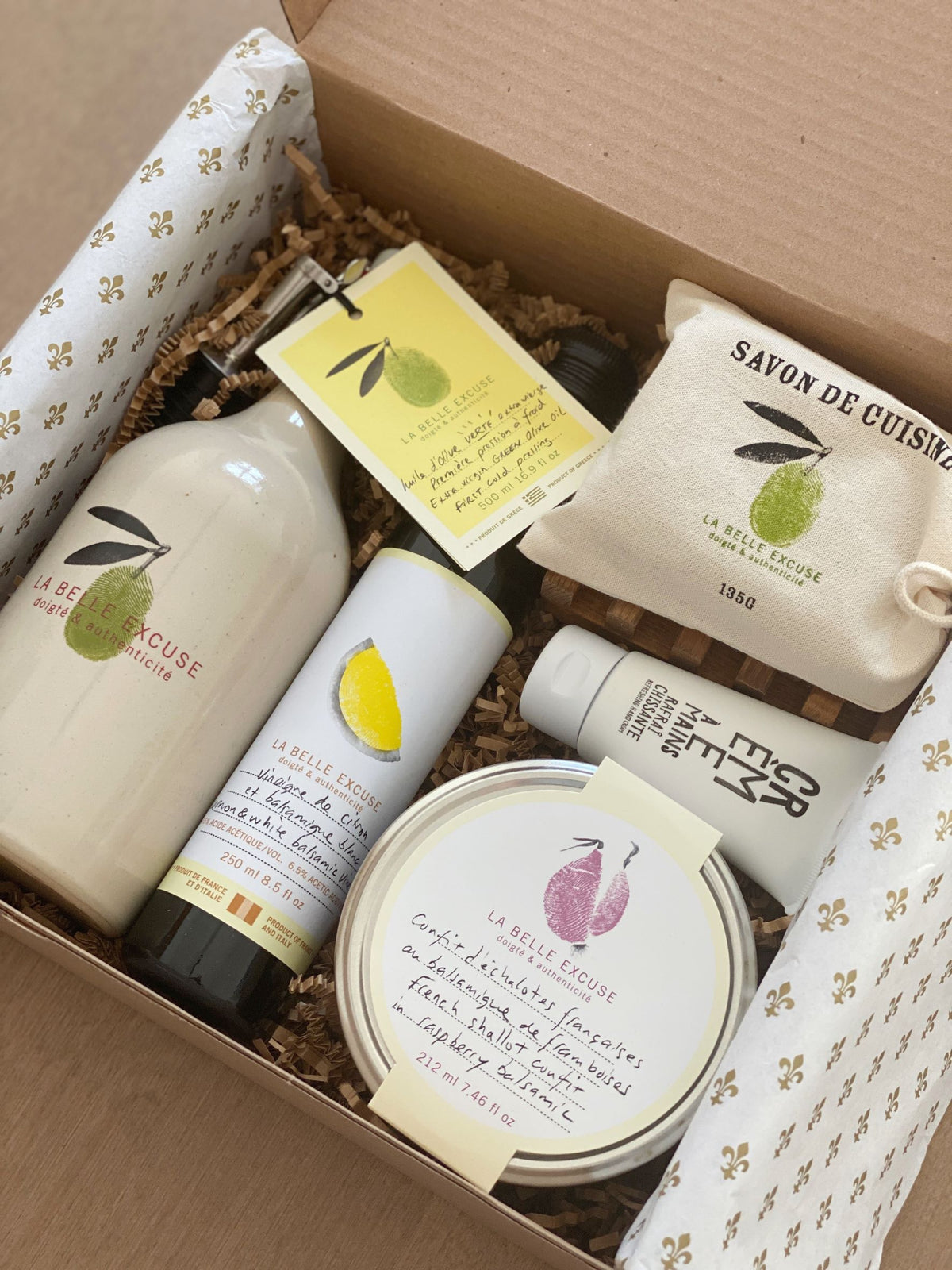 La Belle Excuse Gourmet Gift Set featuring a ceramic cruet filled with green olive oil, lemon and white balsamic vinegar, French shallot confit, kitchen soap with a soap dish, and olive oil hand cream.