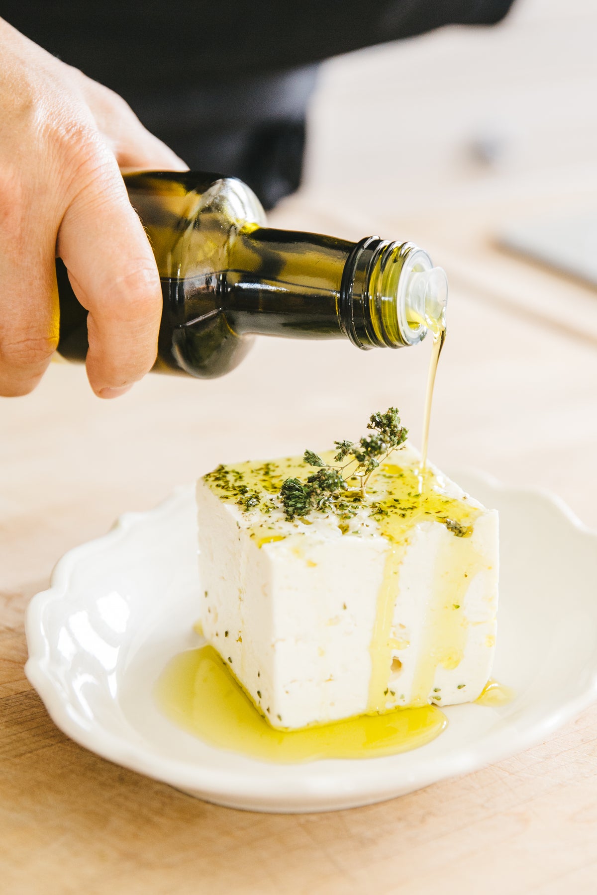 Person pouring La Belle Excuse extra virgin olive oil over a block of feta cheese on a white plate.