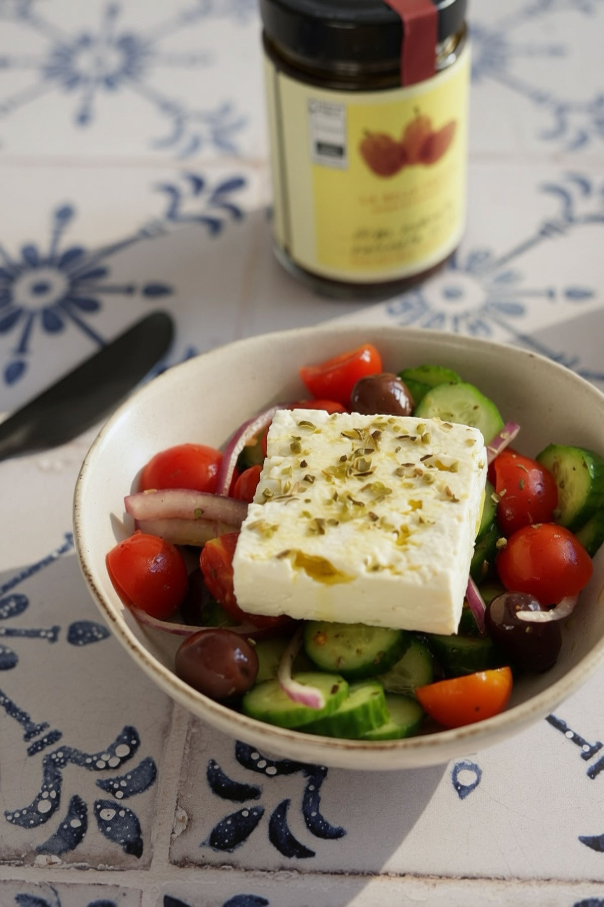 Greek salad with feta cheese on a decorative table with La Belle Excuse Kalamata olives from Greece, available in 180 g, 340 g, and 2 kg formats.
